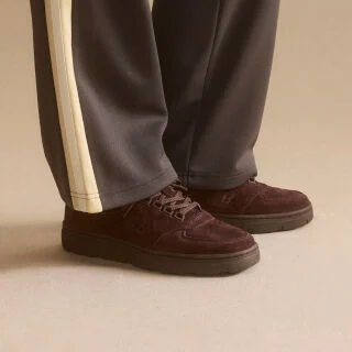 Knee down view of a man wearing a pair of New Balance Made in UK sneakers standing on a patterned tile floor.  