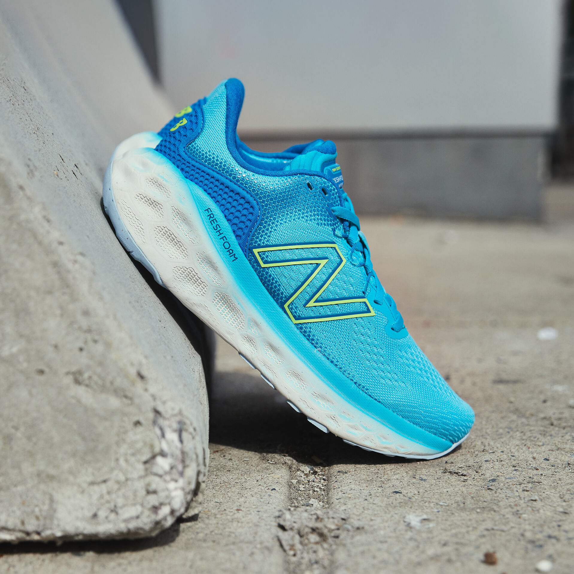 Slide profile of light blue Fresh Foam More v3 shoes resting heels against a concrete block