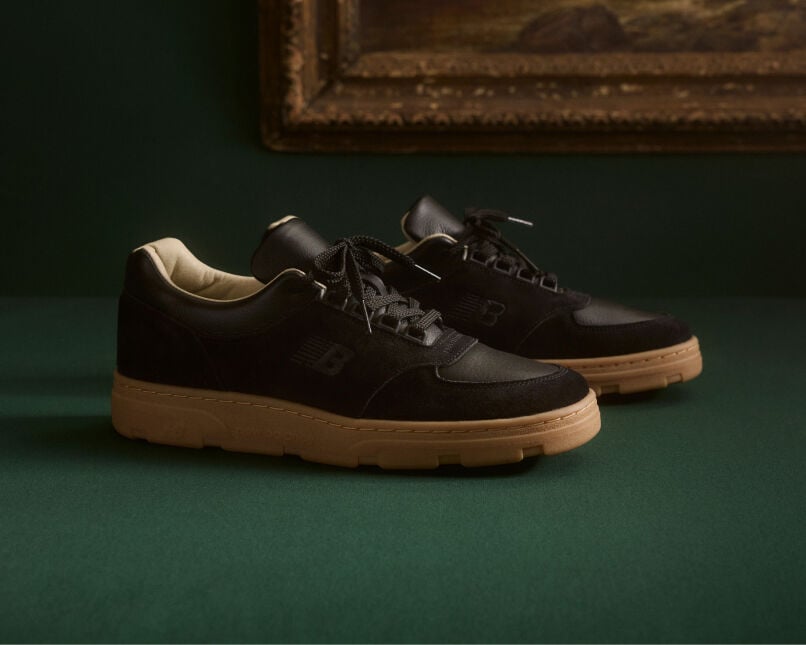 Knee down view of a man wearing a pair of New Balance Made in UK sneakers standing on a patterned tile floor.  