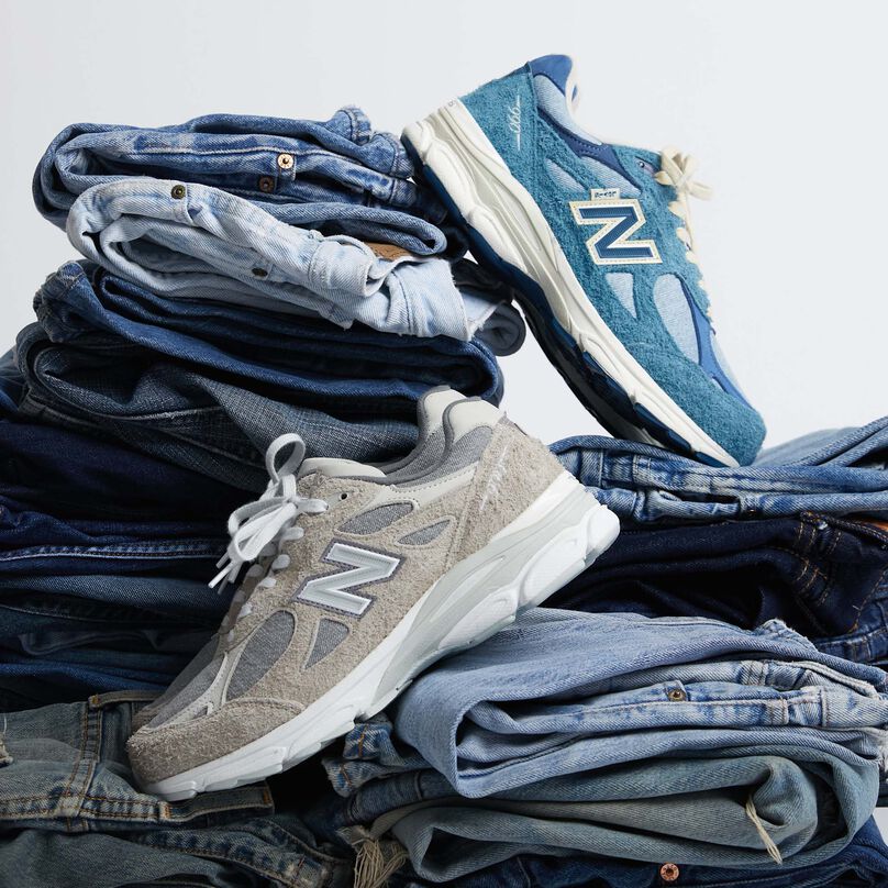 2 pair of 990v3 shoes, one grey and one blue, propped up against multiple piles of Levi’s® jeans