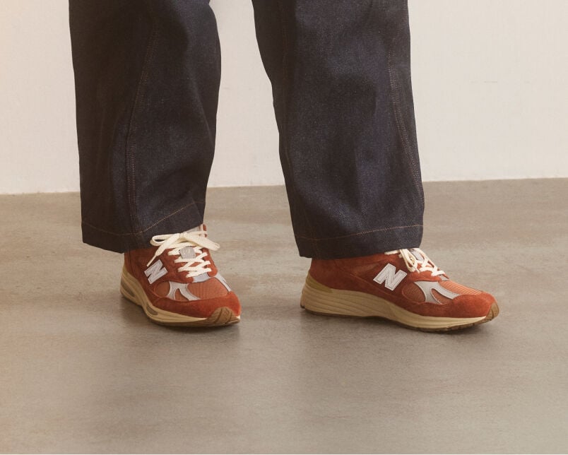 A pair of New Balance Made in UK sneakers in front of a rabbit in a brown textured studio environment. 
