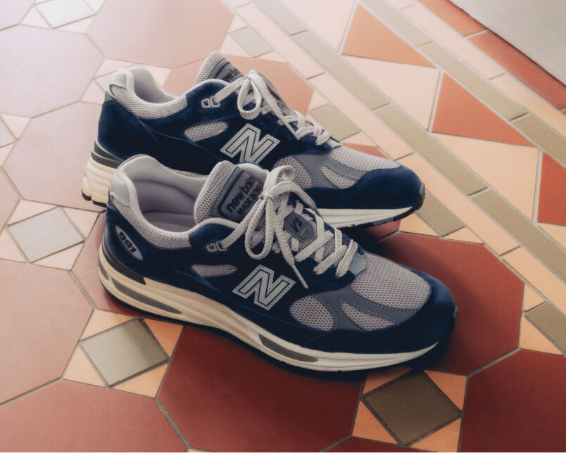 A pair of New Balance Made in UK sneakers in front of a rabbit in a brown textured studio environment. 