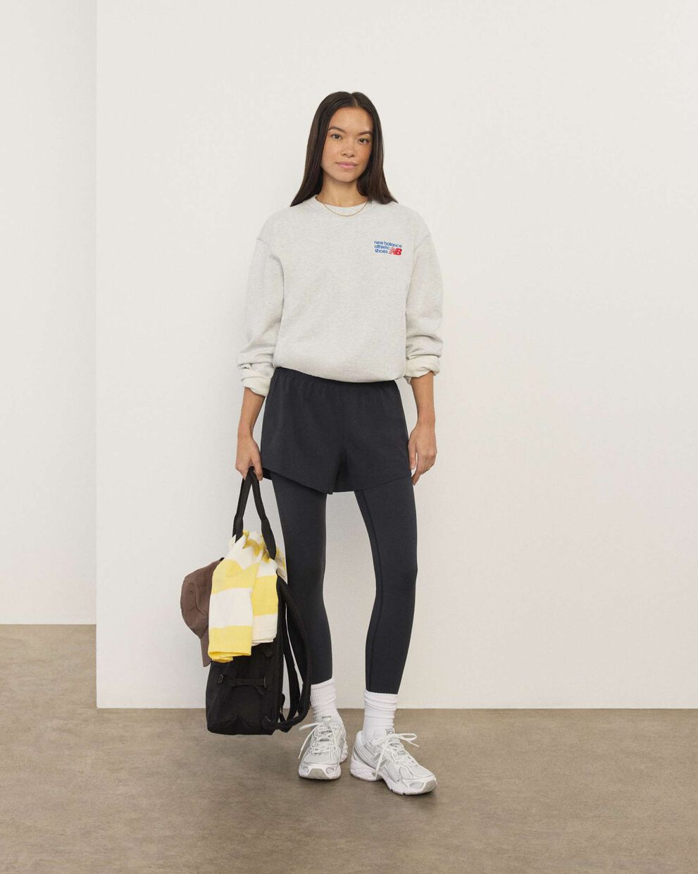 A woman wearing New Balance standing in front a white wall.