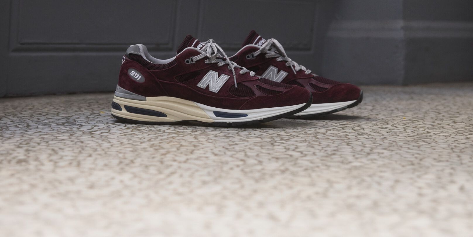 A pair of New Balance Made in UK sneakers sitting on a concrete floor.