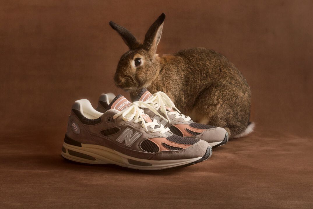 Feet view of a woman wearing a pair of New Balance Made in UK sneakers standing on a white tiled floor.