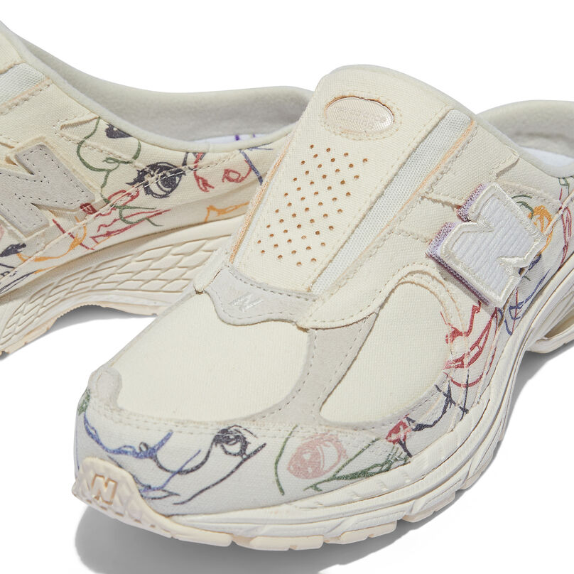 Cropped view of the upper a cream colored mule shoe with embroidered art on th