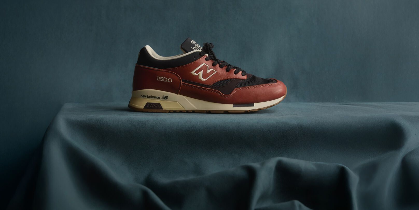 A New Balance Made in UK sneaker sitting in a flowing blue fabric studio backdrop. 